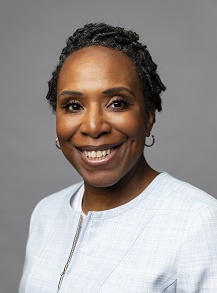 Chisa smiling at the camera with a white top on against a grey background